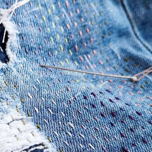 Réparation de jeans à l'aide de points de couture. Une toile de jean bleue et une aiguille.