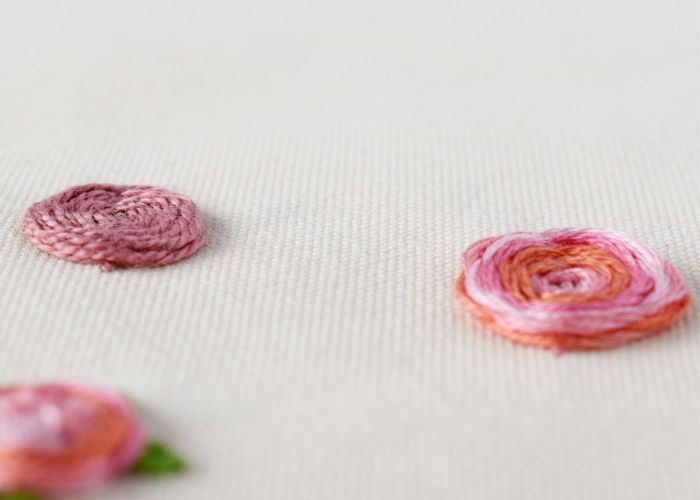 Fleurs roses brodées à la main au point de roue sur tissu blanc